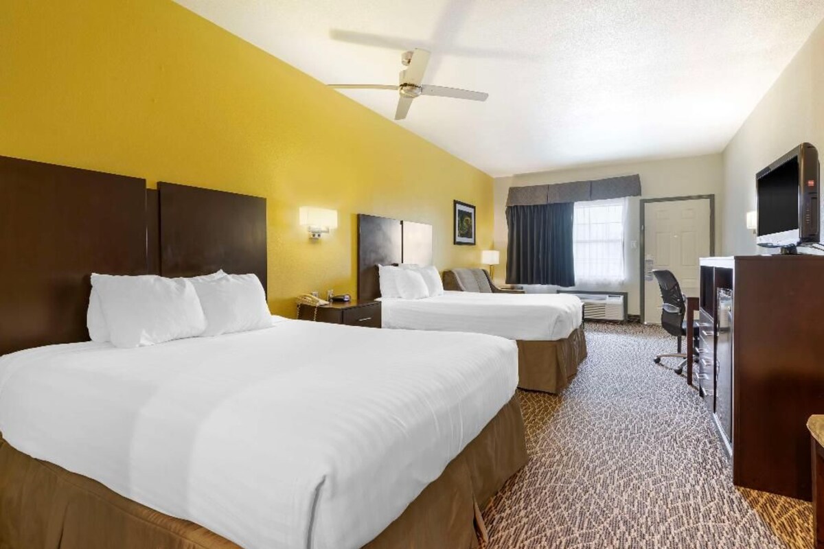 A hotel room with two beds, a desk, a television, and a ceiling fan.