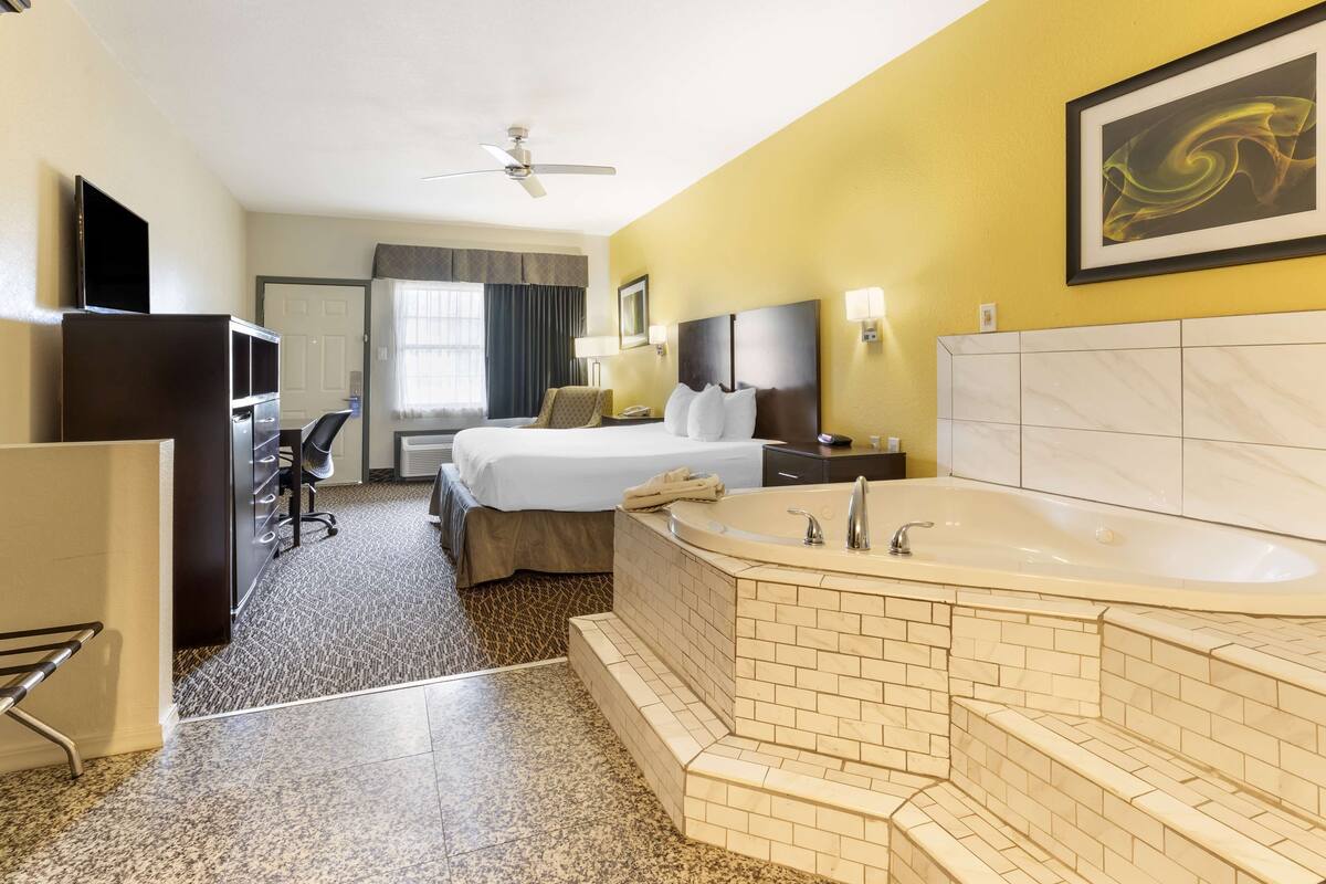 A hotel room with a bed, a desk, a television, a bathroom with a bathtub, and a ceiling fan.