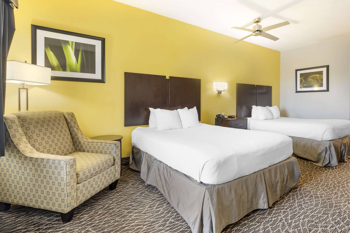 A hotel room with two beds, a chair, a ceiling fan, and a lamp.