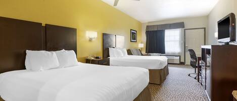 A hotel room with two beds, a desk, a television, and a ceiling fan.