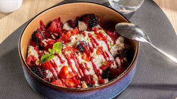 A bowl of dessert with berries and cream, placed on a table with a water glass and a napkin.