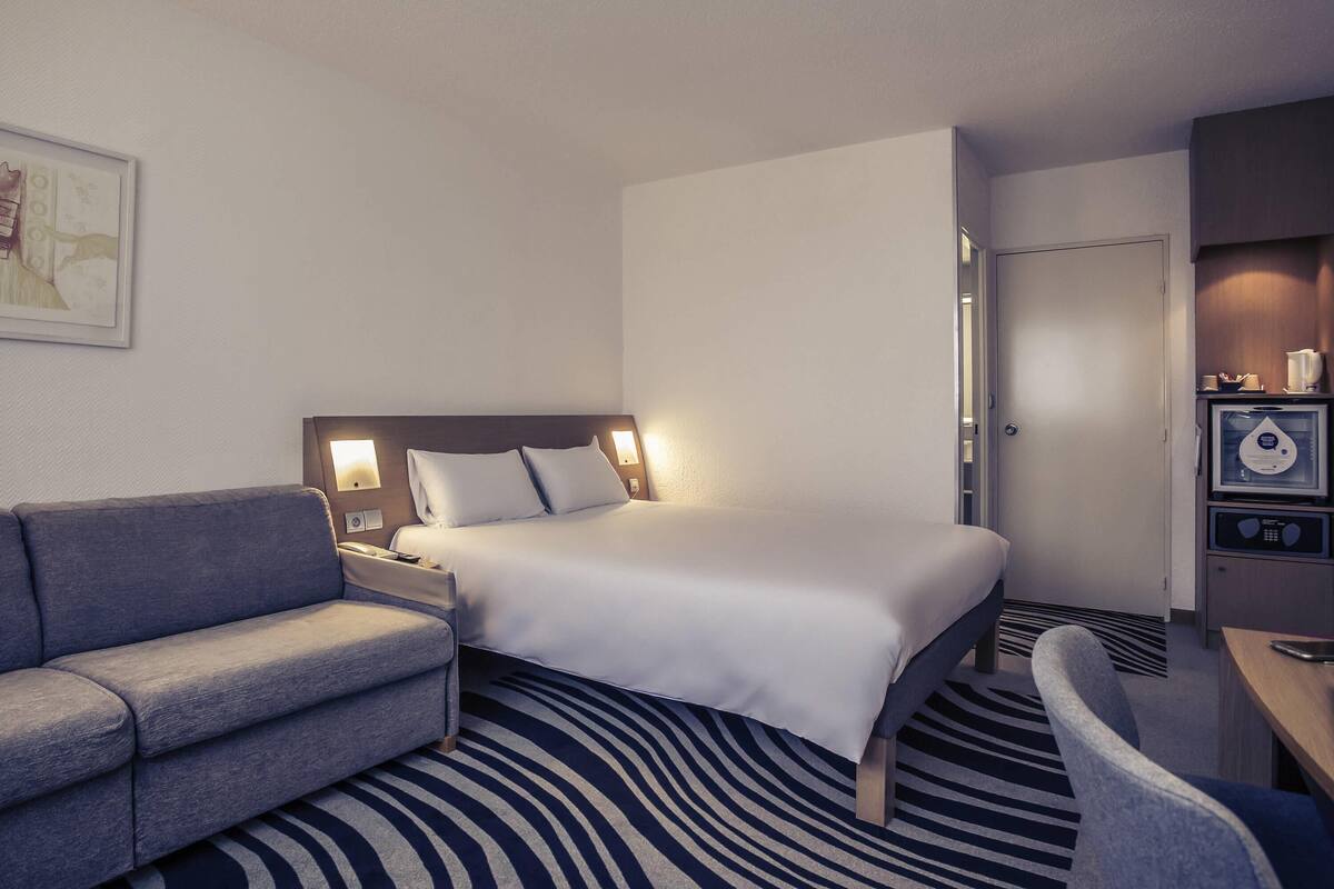 A hotel room with a bed, a sofa, a desk, and a microwave.