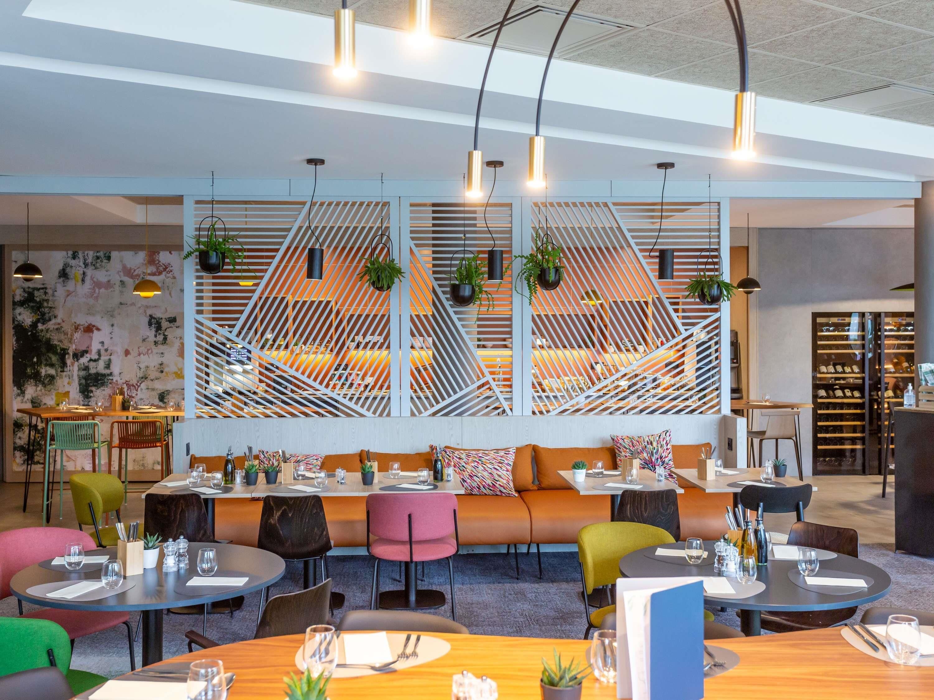 Een modern restaurantinterieur met een centraal zitgedeelte, meerdere tafels en hangplanten.