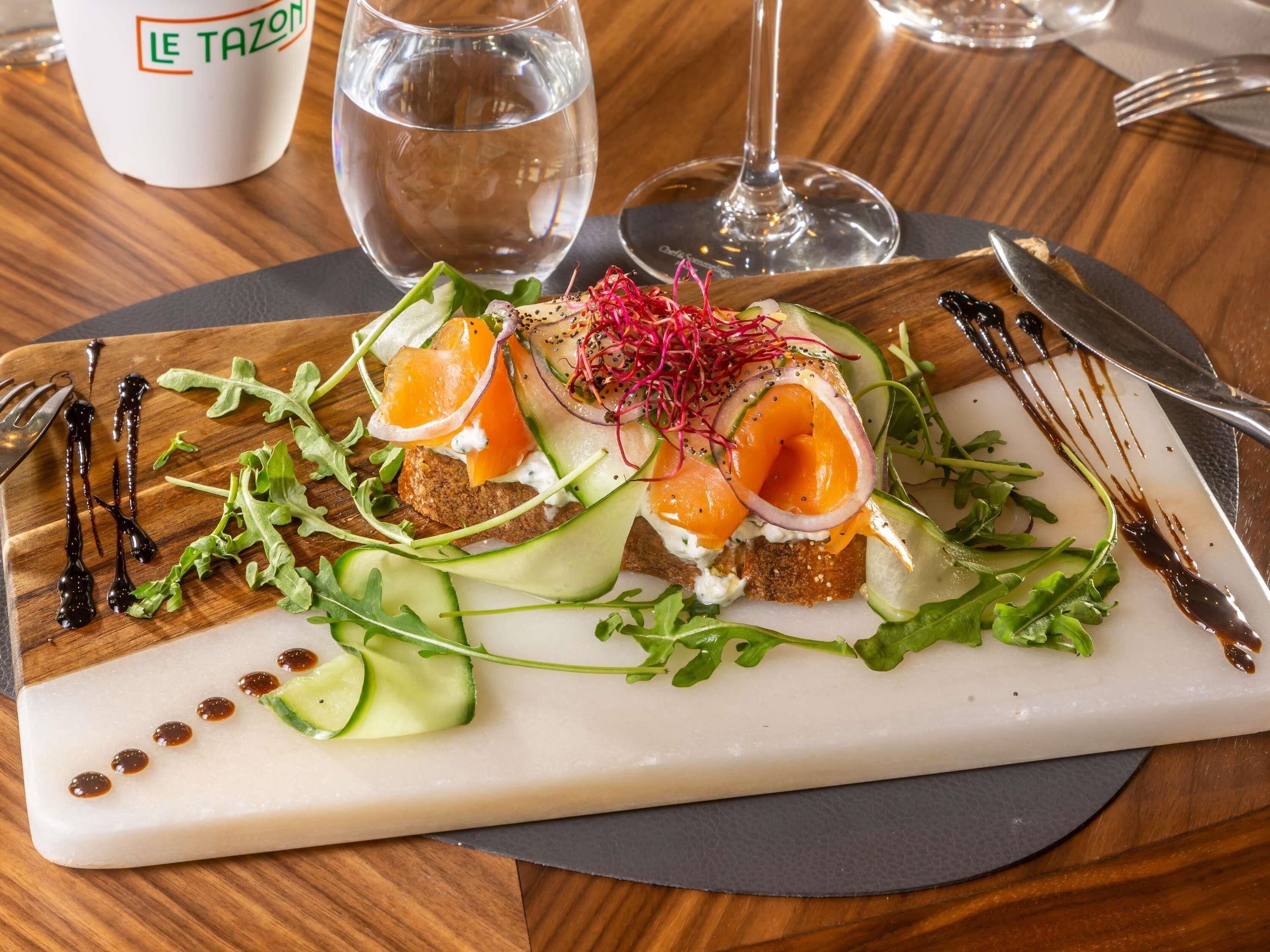 Une assiette contenant du saumon, des légumes verts et une sauce blanche, accompagnée d’un verre d’eau et d’un verre à vin, le tout posé sur une table en bois.