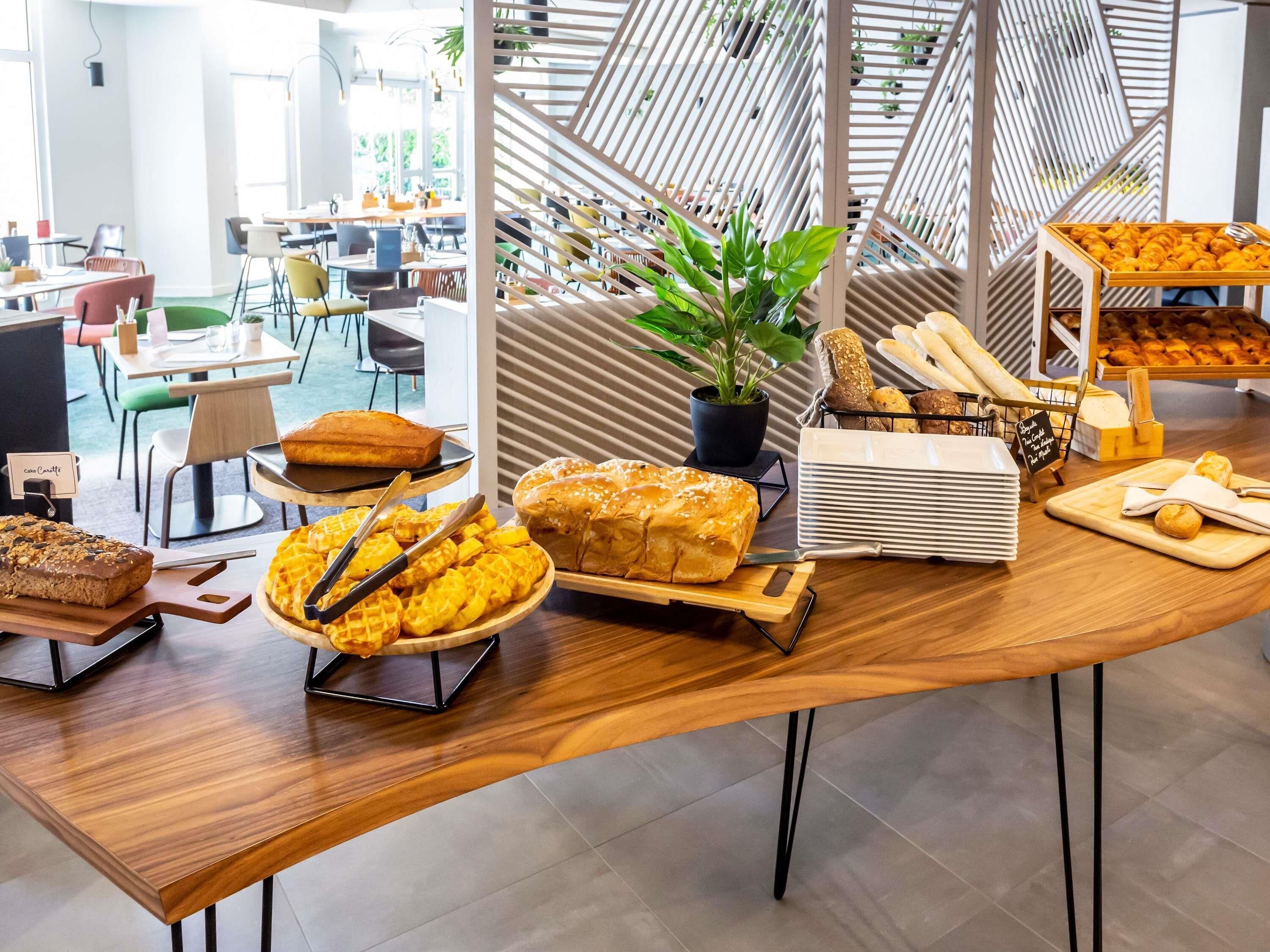 Una mesa de buffet con diferentes productos de panadería y una planta en maceta.