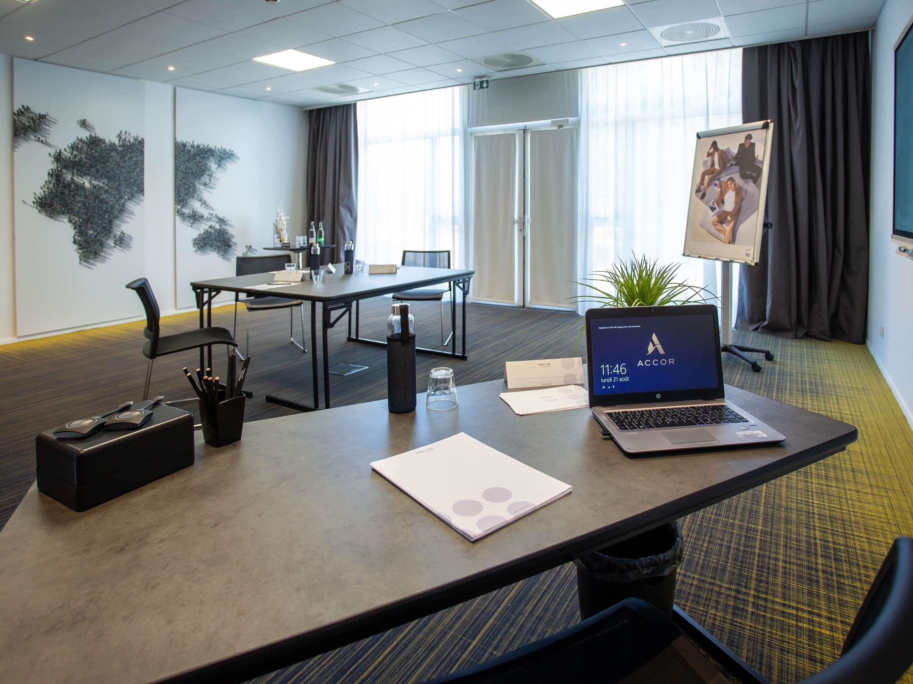A conference room with a laptop, a notebook, and a pen holder on a table.
