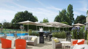 An outdoor patio area with seating, umbrellas, and a pool in the background.