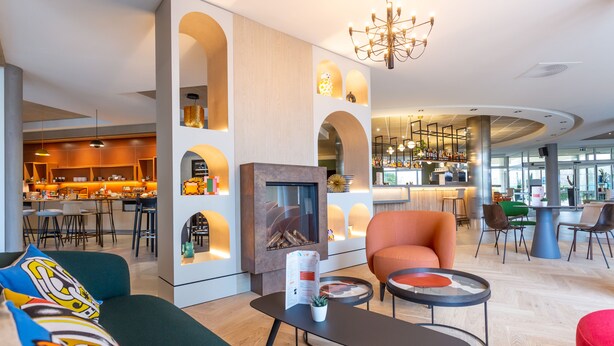 A modern hotel lobby with a fireplace, seating area, and a bar.