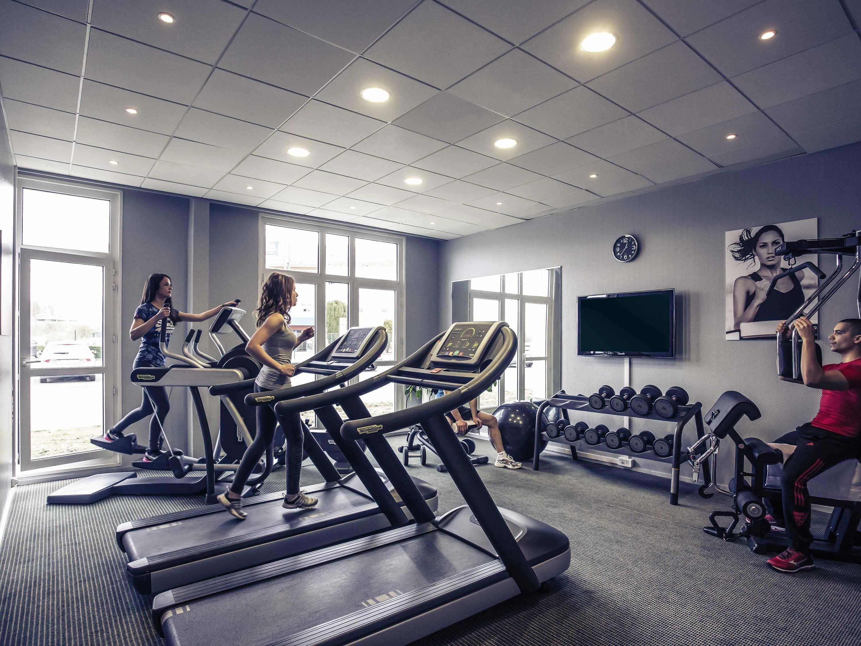 Un gimnasio con cintas de correr, pesas y un televisor en la pared.
