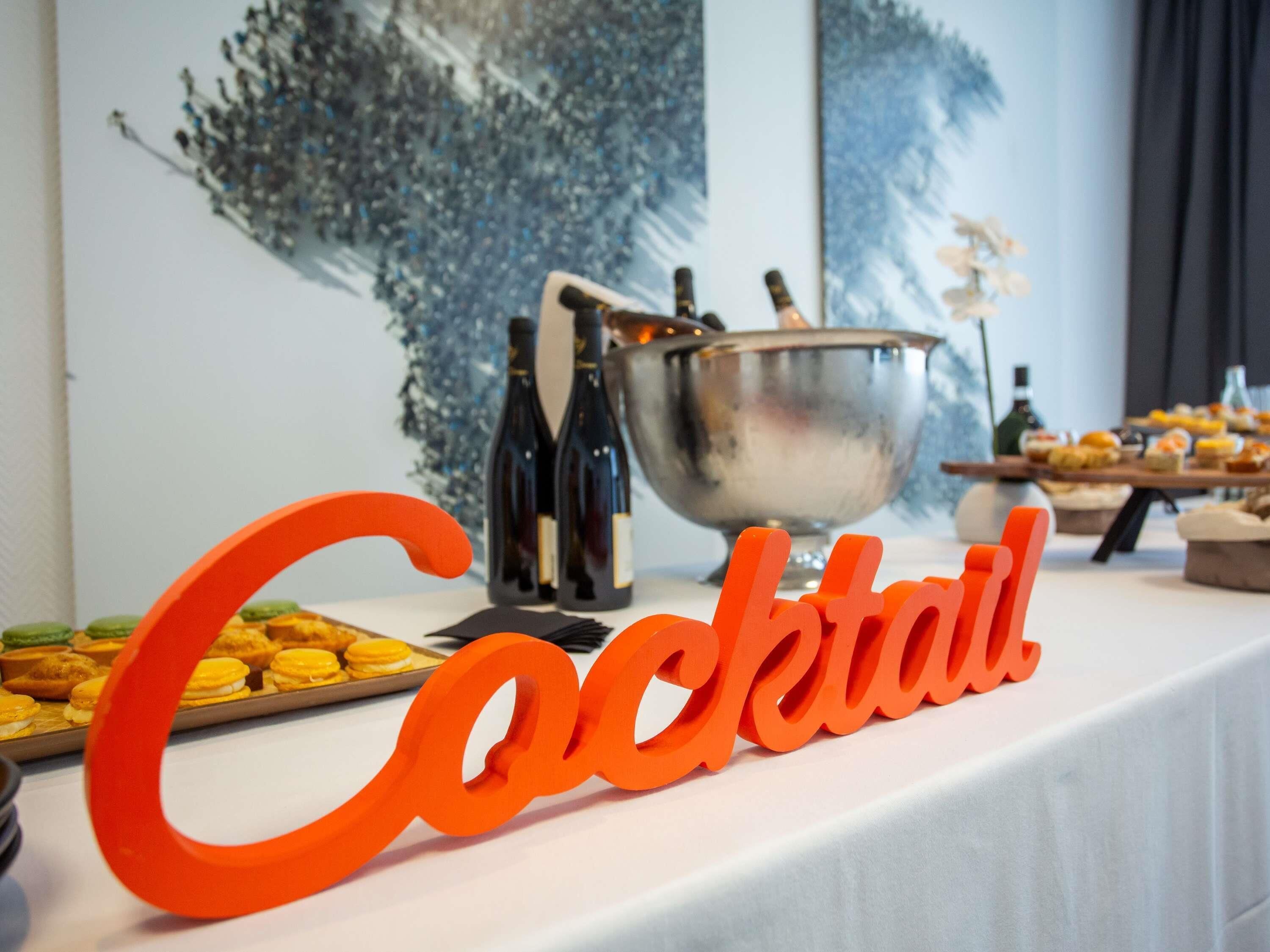 A cocktail station with a sign, a silver bowl, wine bottles, and various snacks.