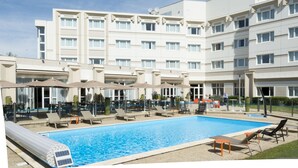 A hotel with a swimming pool, outdoor seating, and a clear sky.