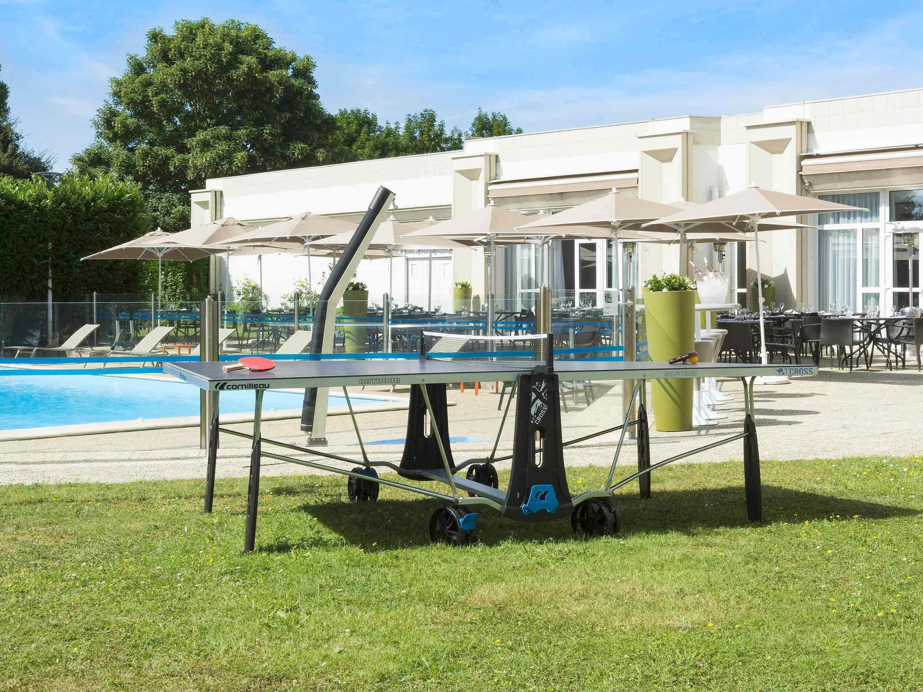 A poolside area with a table tennis table, outdoor seating, and a building in the background.