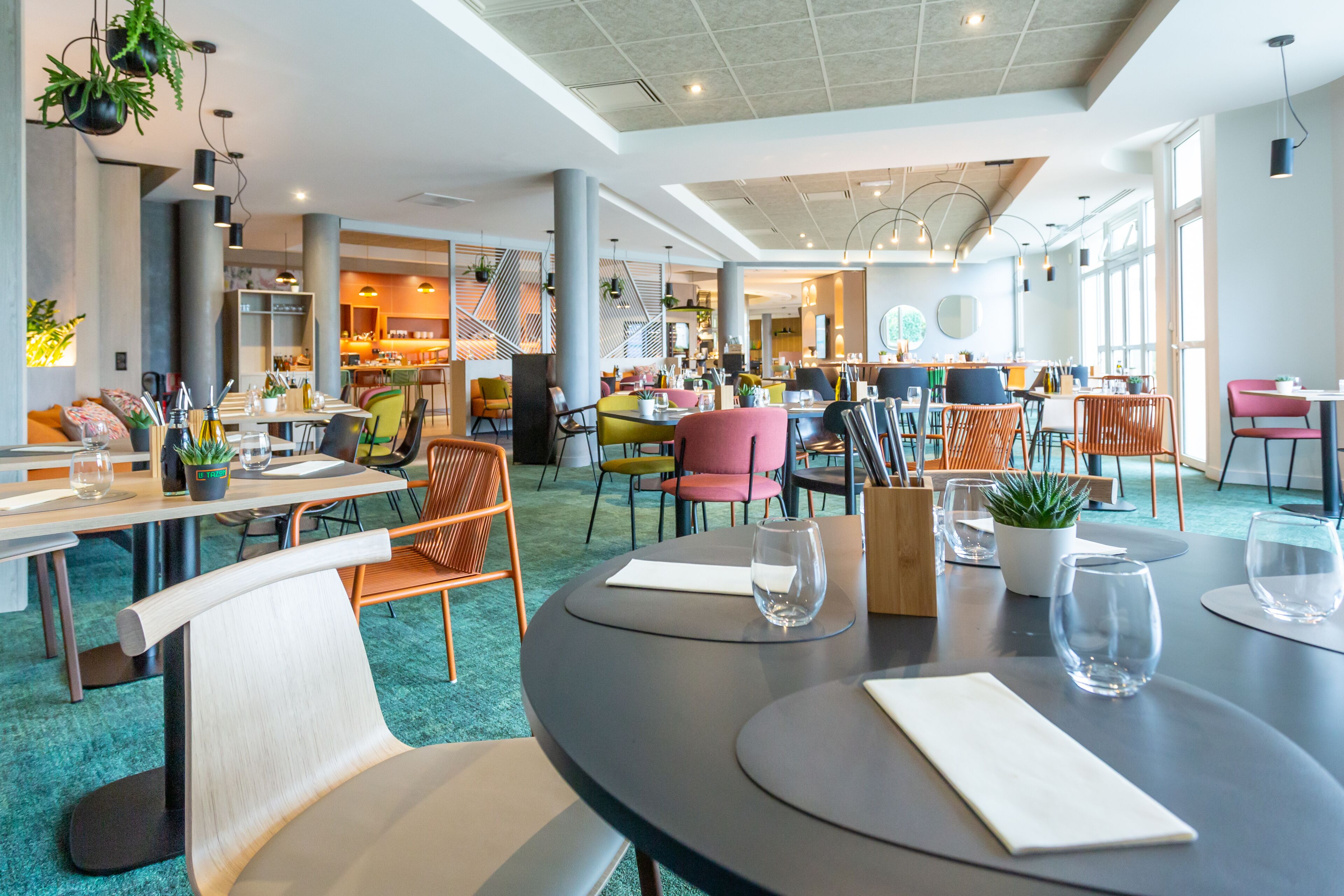 Un restaurante moderno con mesas redondas, sillas coloridas y plantas en macetas.