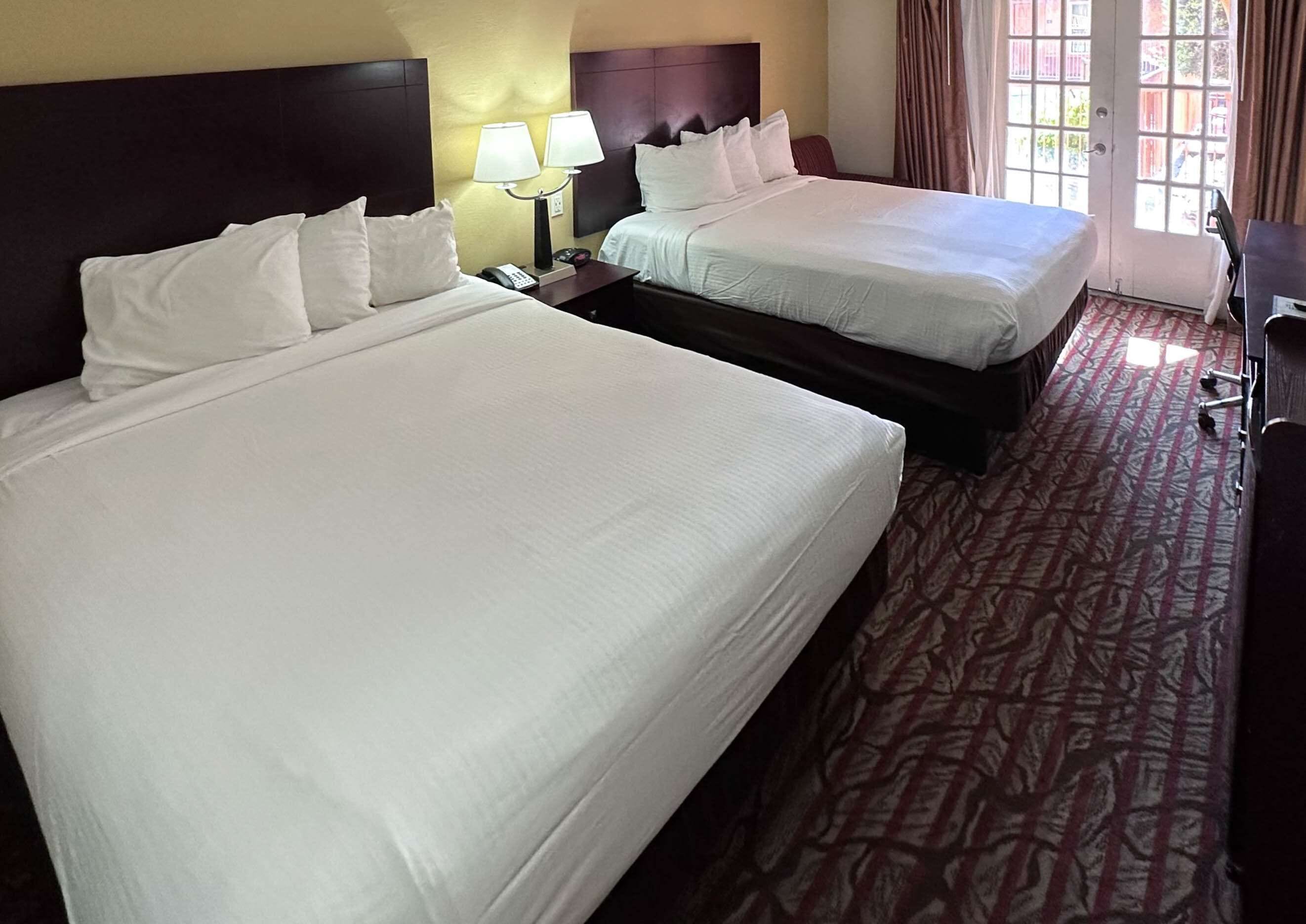 A hotel room with two beds, a nightstand with a lamp, and a patterned carpet.