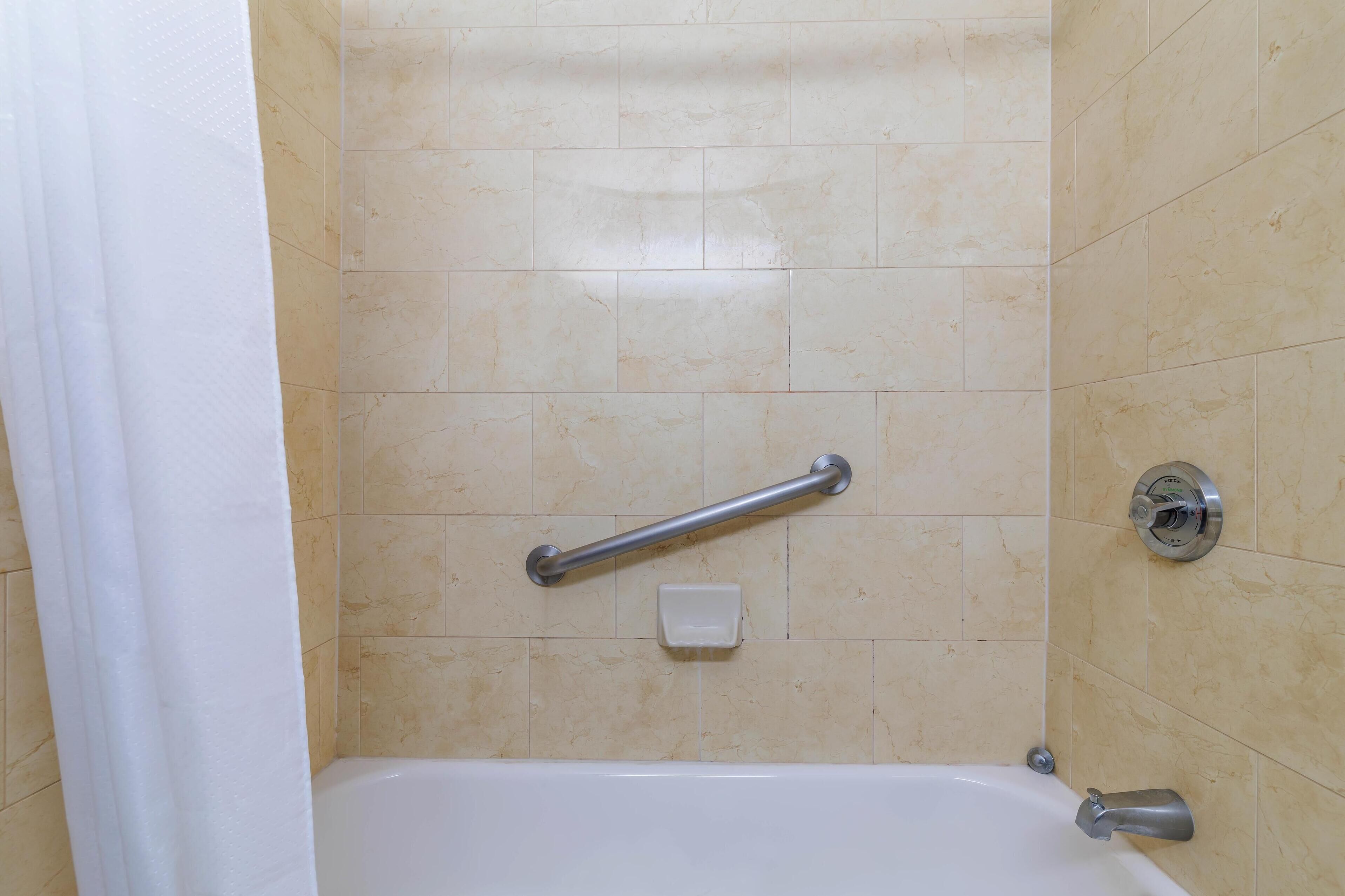 A bathroom with a bathtub, a handrail, a soap dish, and a shower curtain.