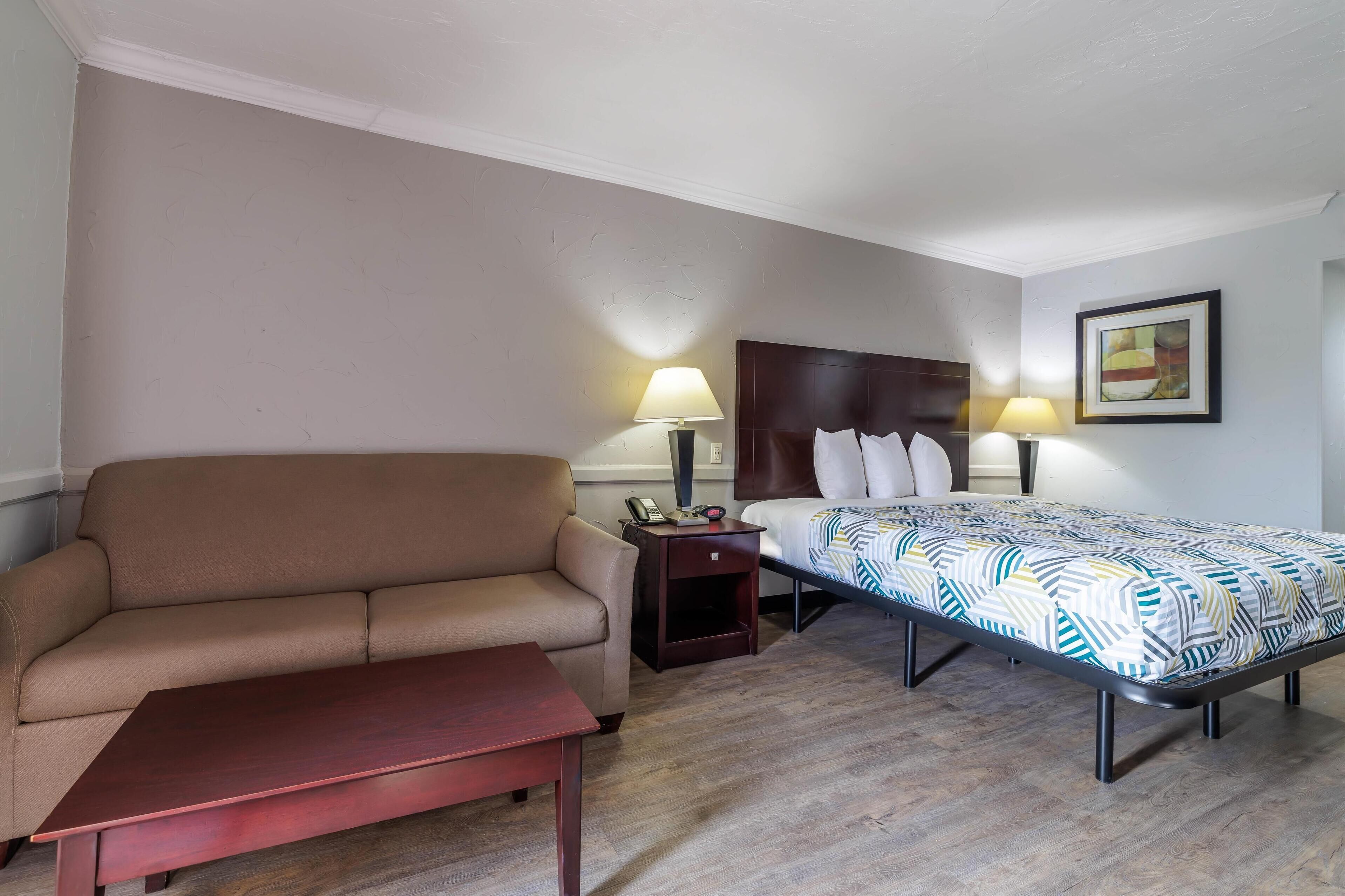 A hotel room with a bed, a sofa, a small table, and two bedside lamps.