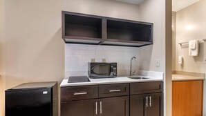 A compact kitchen with dark cabinets, a microwave, a sink, and a small refrigerator.