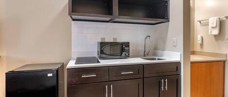 A compact kitchen with dark cabinets, a microwave, a sink, and a small refrigerator.