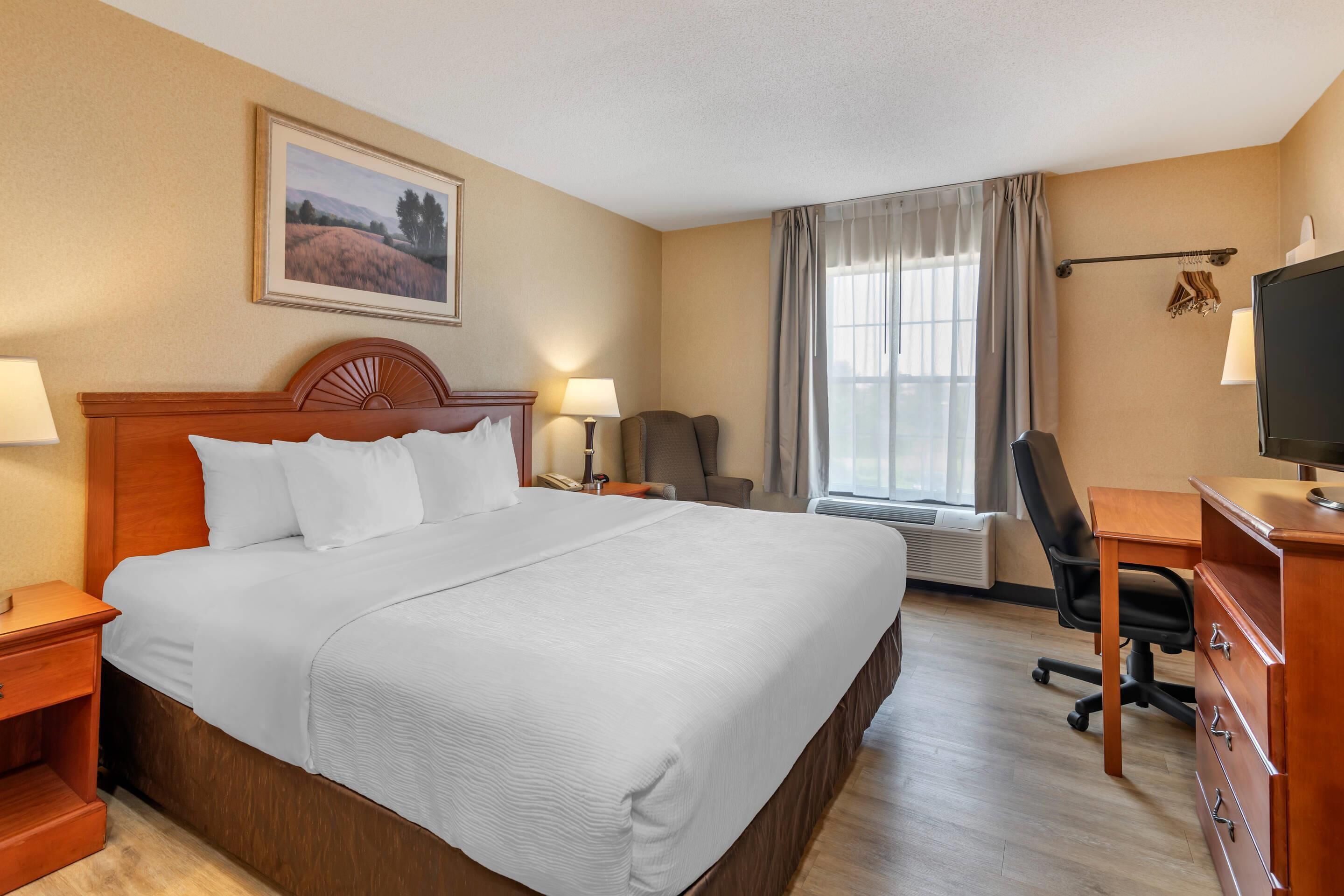 A hotel room with a large bed, a desk with a computer, a chair, a TV, and a window with curtains.