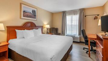 A hotel room with a large bed, a desk with a computer, a chair, a TV, and a window with curtains.