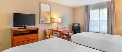 A hotel room with two beds, a TV, a desk with a lamp, a mirror, and a window with curtains.