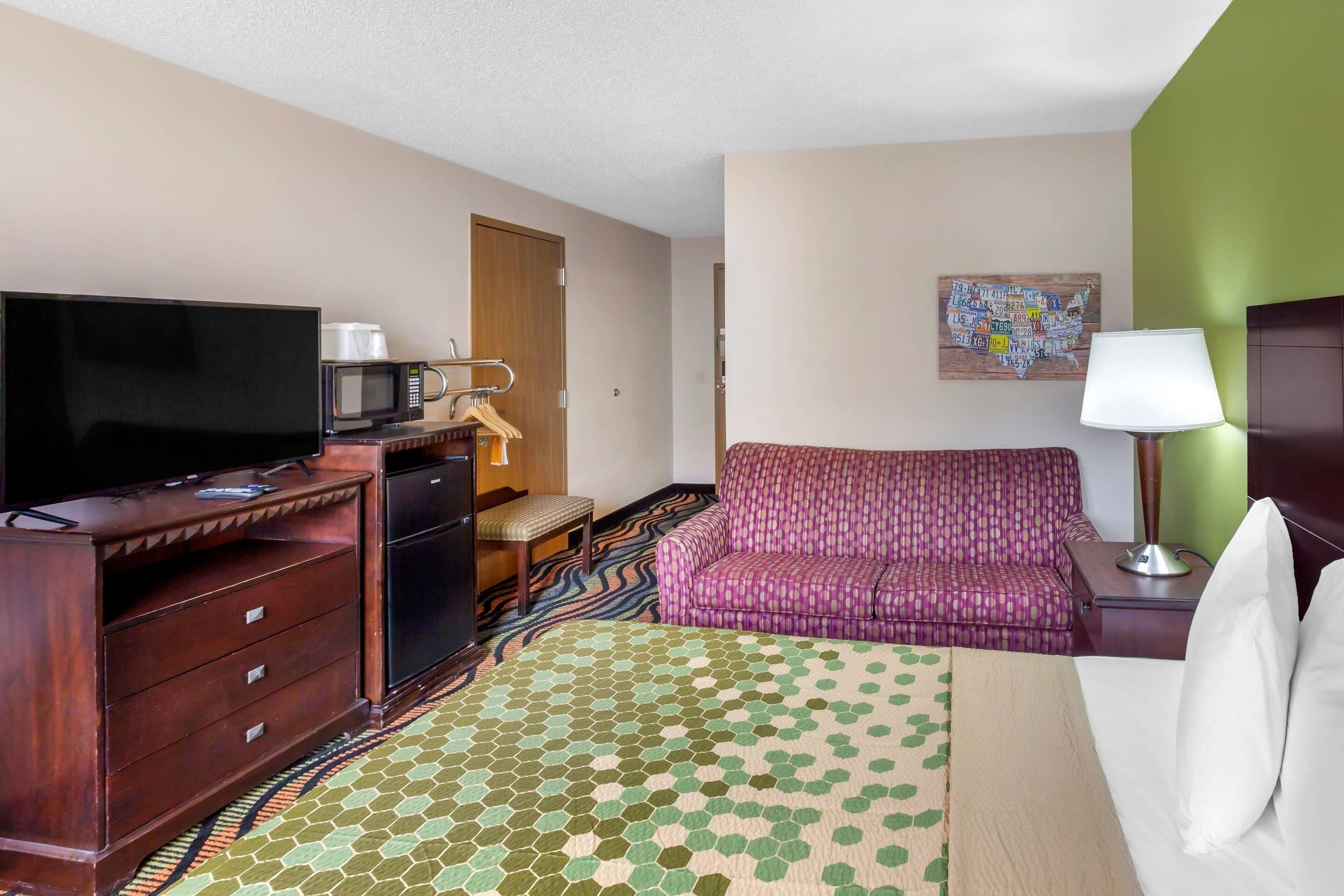 A hotel room with a television, a microwave, a sofa, a bed, a desk, and a dresser.