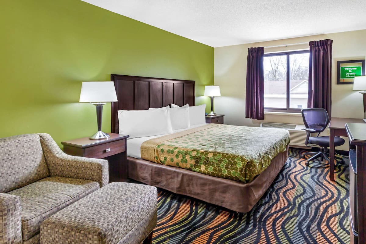 A hotel room with a bed, two chairs, a desk, a lamp, and a window with curtains.