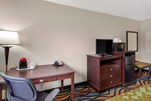 A hotel room with a desk, chair, lamp, telephone, television, microwave, refrigerator, and a patterned rug. - Econo Lodge Inn & Suites Oconto (Oconto)