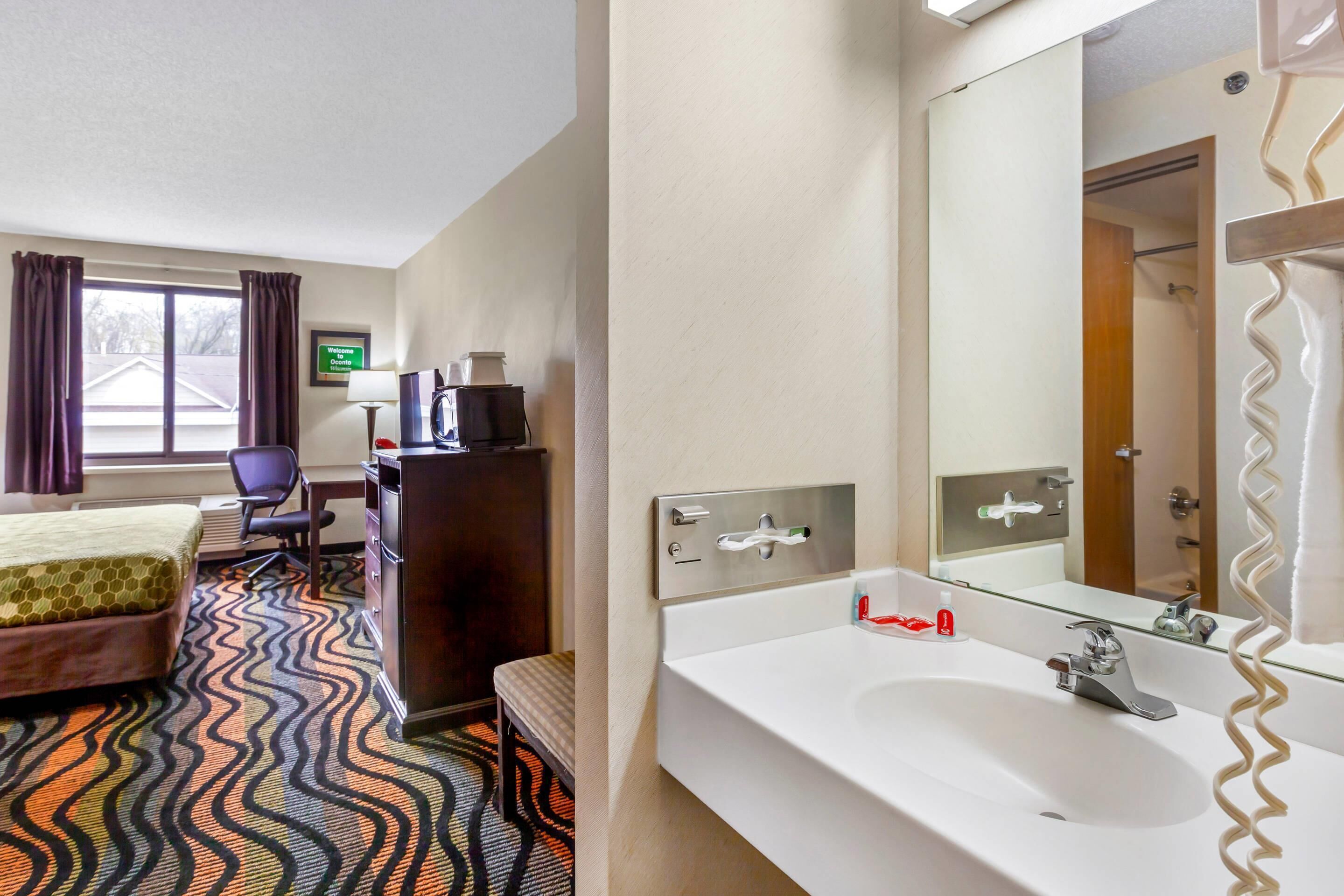 Une chambre d’hôtel comprenant un lit, un bureau, une chaise et une grande salle de bain avec un lavabo et un miroir.