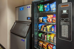 A vending machine stocked with various snacks and a small refrigerator.