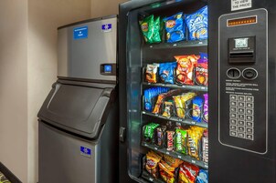 A vending machine stocked with various snacks and a small refrigerator.