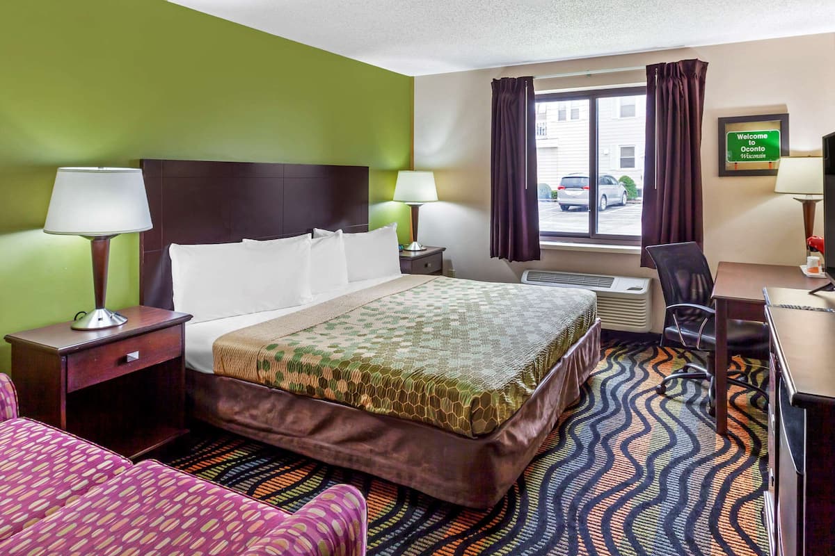 A hotel room with a bed, two bedside tables with lamps, a desk with a chair, and a window with curtains.