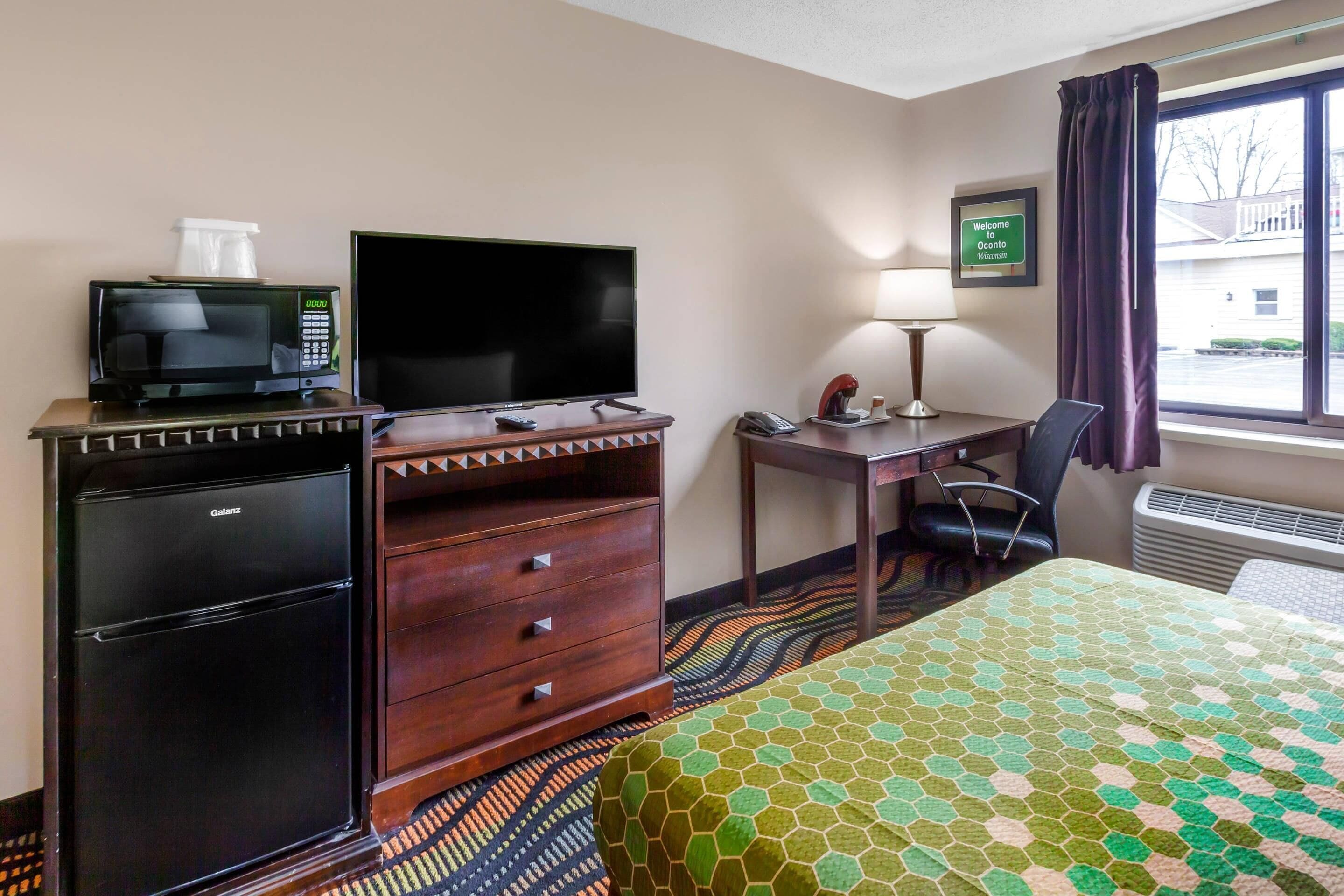 Una camera d'albergo con un letto, una scrivania, una televisione, un minibar e una finestra vista esterna.