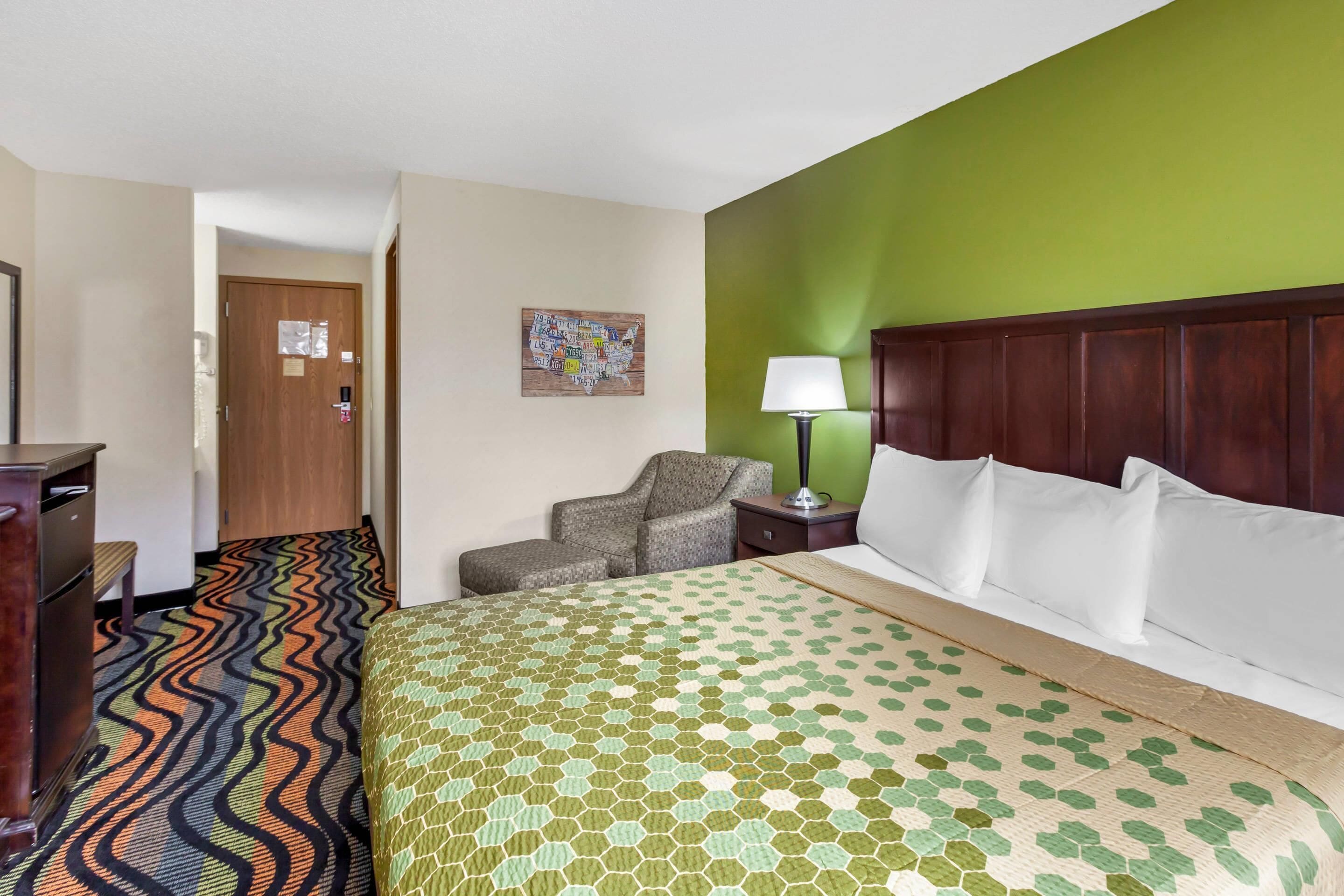 A hotel room with a bed, a chair, a desk, and a lamp.