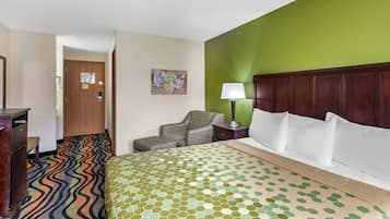 A hotel room with a bed, a chair, a desk, and a lamp.