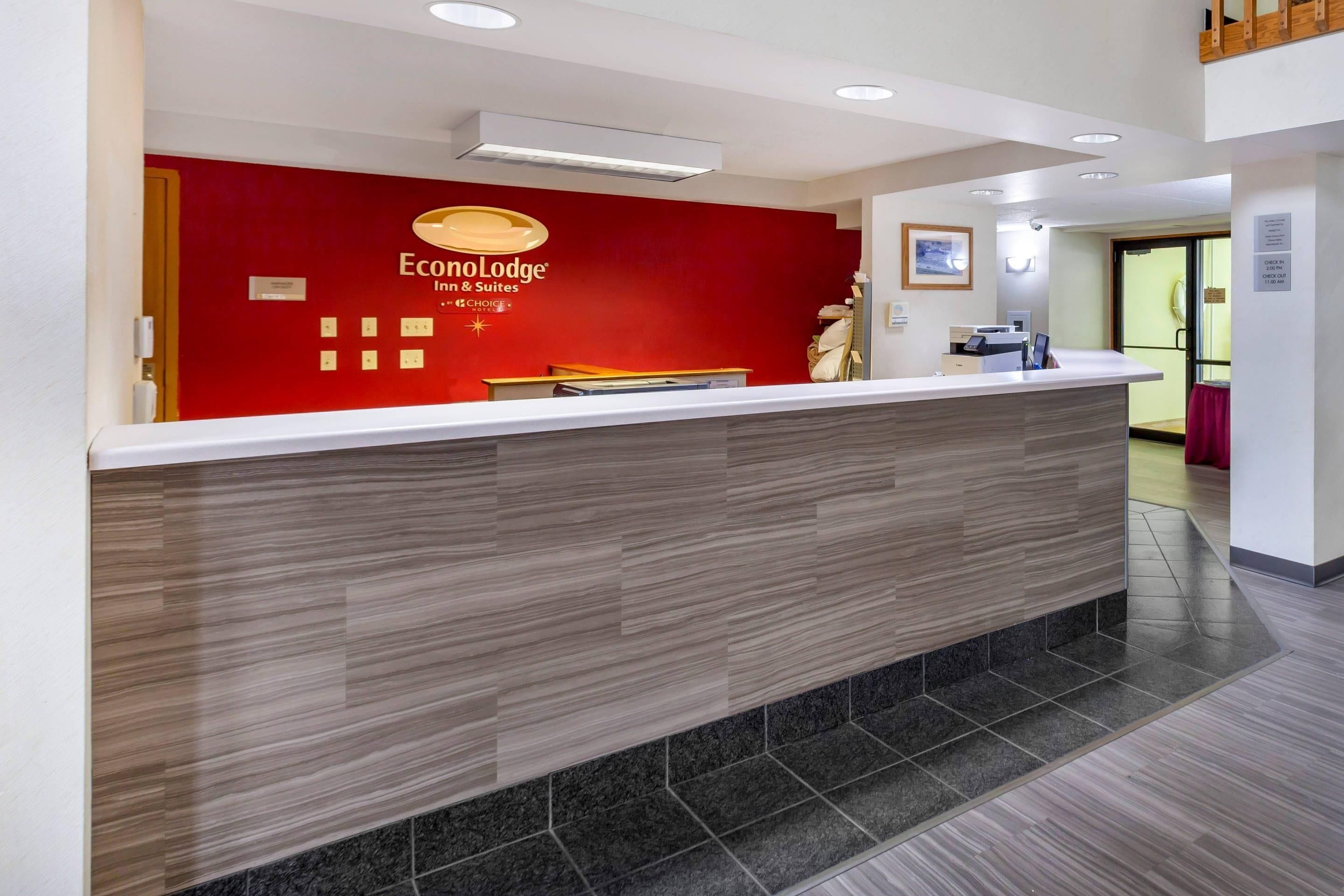 A reception desk with a red wall, a wooden counter, and a check-in/out sign.