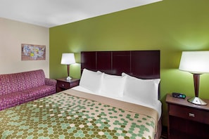 A hotel room with a bed, a green wall, a purple sofa, and a nightstand with a lamp. - Econo Lodge Inn & Suites Oconto (Oconto)