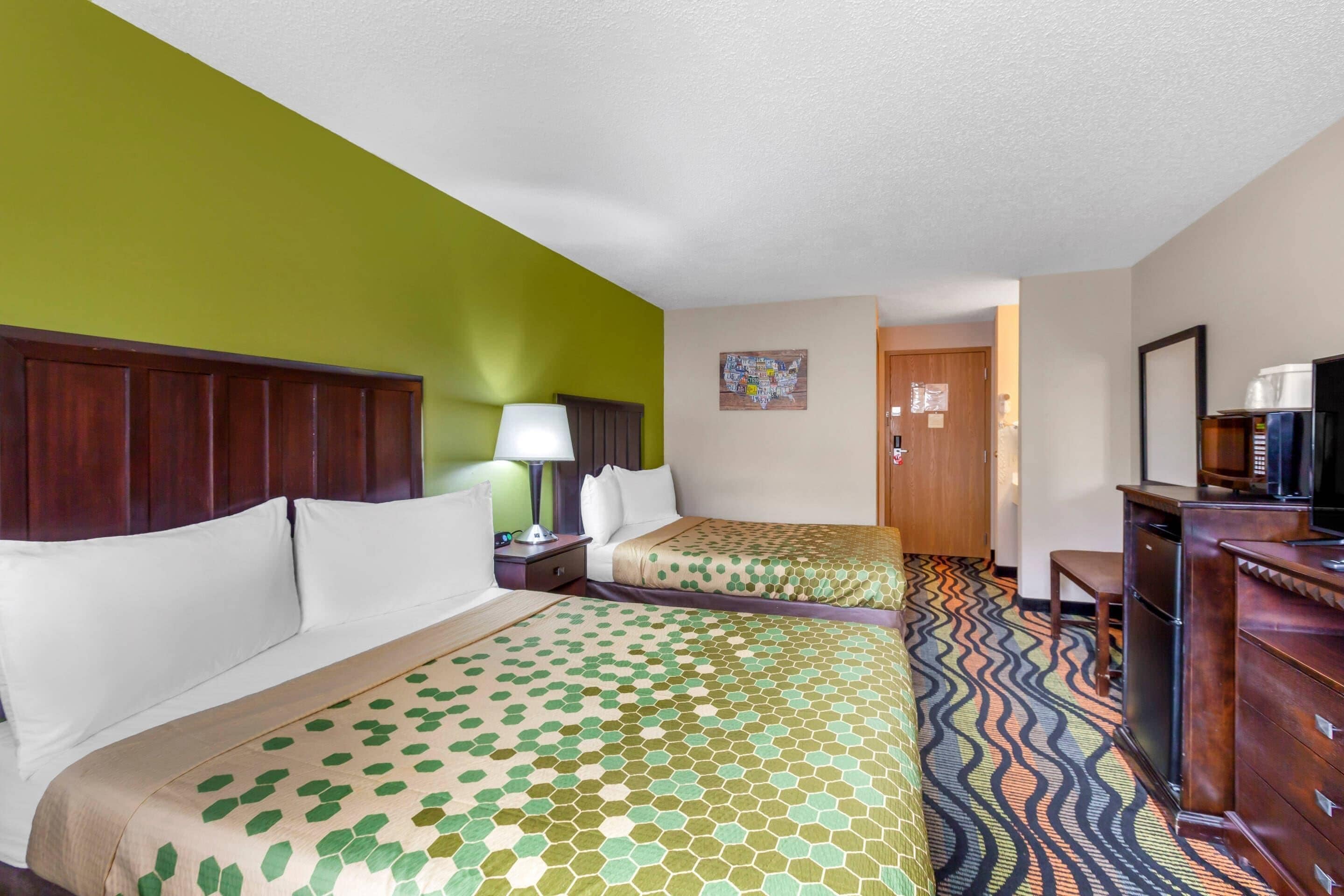 Una habitación de hotel con dos camas, un escritorio, un televisor y una alfombra estampada.