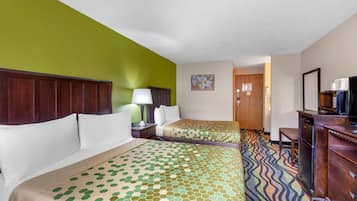 Una habitación de hotel con dos camas, un escritorio, un televisor y una alfombra estampada.