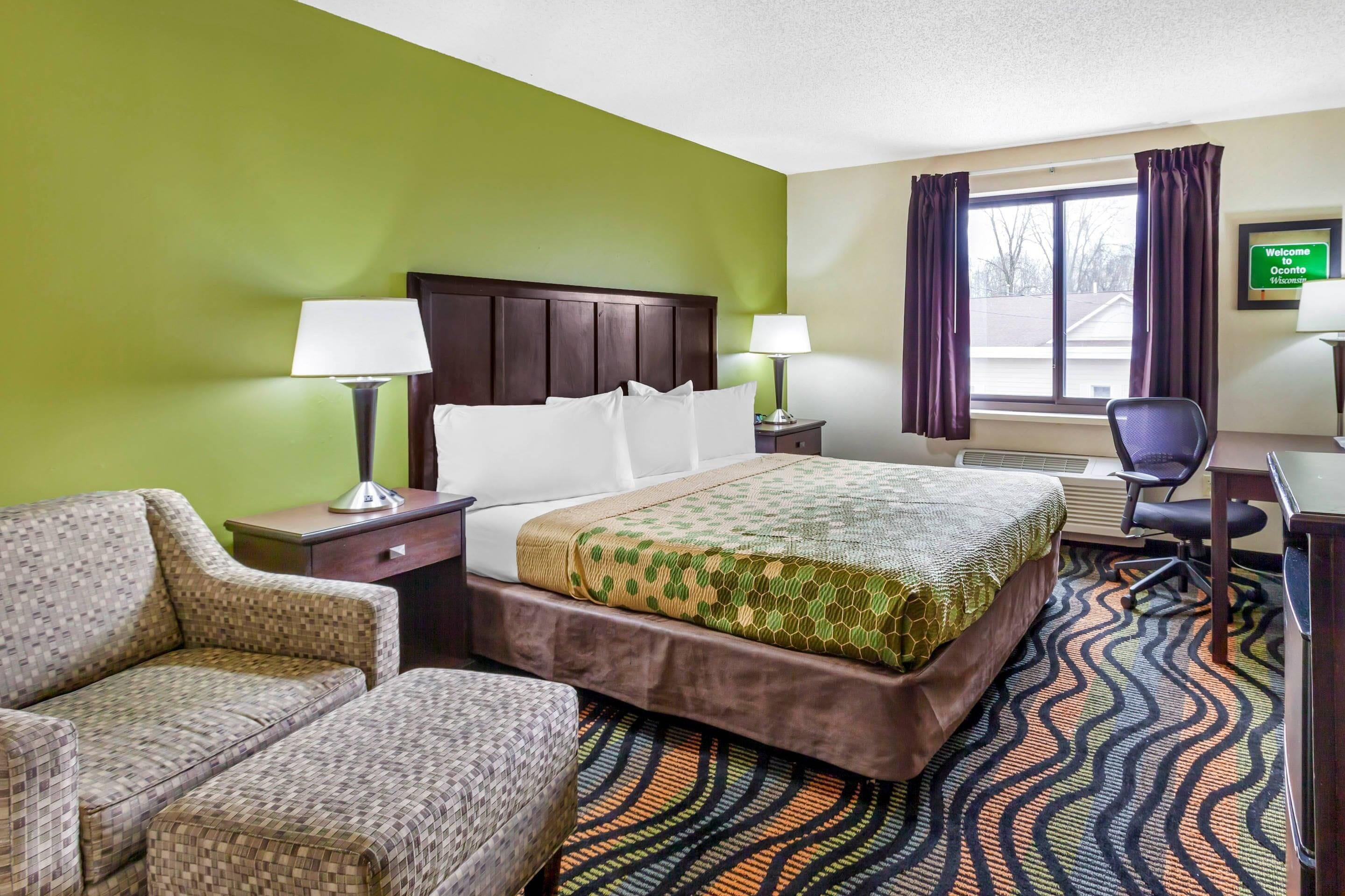 A hotel room with a bed, two nightstands, a desk, a chair, and a view of the outdoors.