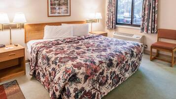 A hotel room with a large bed, two bedside lamps, a nightstand, a chair, a window with curtains, and a radiator.