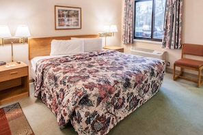 A hotel room with a large bed, two bedside lamps, a nightstand, a chair, a window with curtains, and a radiator. - Econo Lodge Inn & Suites Oconto (Oconto)