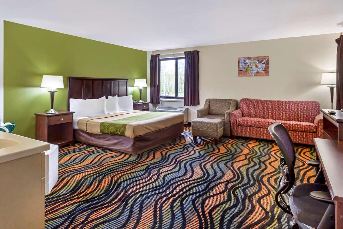 A hotel room with a bed, a desk, a chair, a sofa, and a patterned carpet.