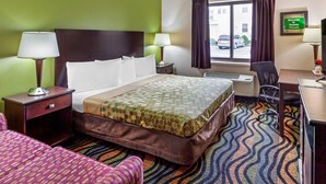 A hotel room with a bed, two bedside lamps, a window with curtains, a desk with a chair, and a 'Welcome to Oconto Wisconsin' sign. - Econo Lodge Inn & Suites Oconto (Oconto)