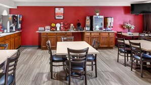 A restaurant with a red wall, a coffee machine, a waffle maker, and a TV mounted on the wall. - Econo Lodge Inn & Suites Oconto (Oconto)