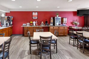 A restaurant with a red wall, a coffee machine, a waffle maker, and a TV mounted on the wall. - Econo Lodge Inn & Suites Oconto (Oconto)