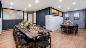 A dining area with a long table set for six, surrounded by dark chairs, with a brick accent wall and framed pictures on the wall. - The Federal Hotel Downtown Carson City, an Ascend Collection Hotel (Carson City)