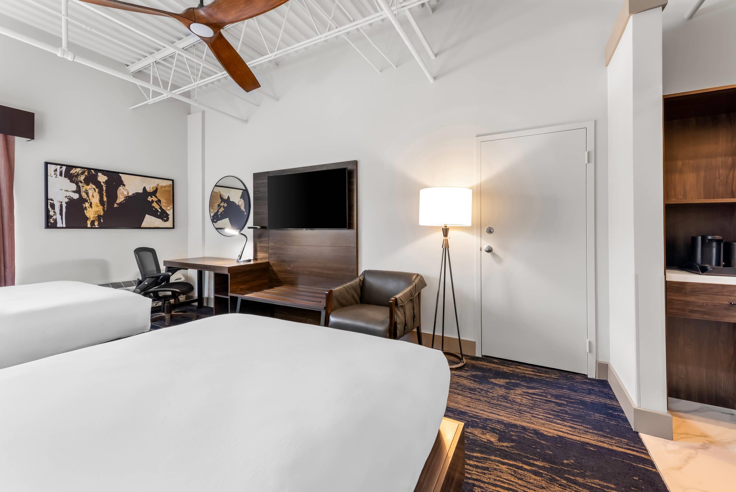 Une chambre d’hôtel avec deux lits, un bureau avec une chaise, une lampe sur pied, une télévision et une armoire.