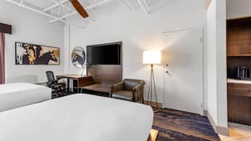 Une chambre d’hôtel avec deux lits, un bureau avec une chaise, une lampe sur pied, une télévision et une armoire.
