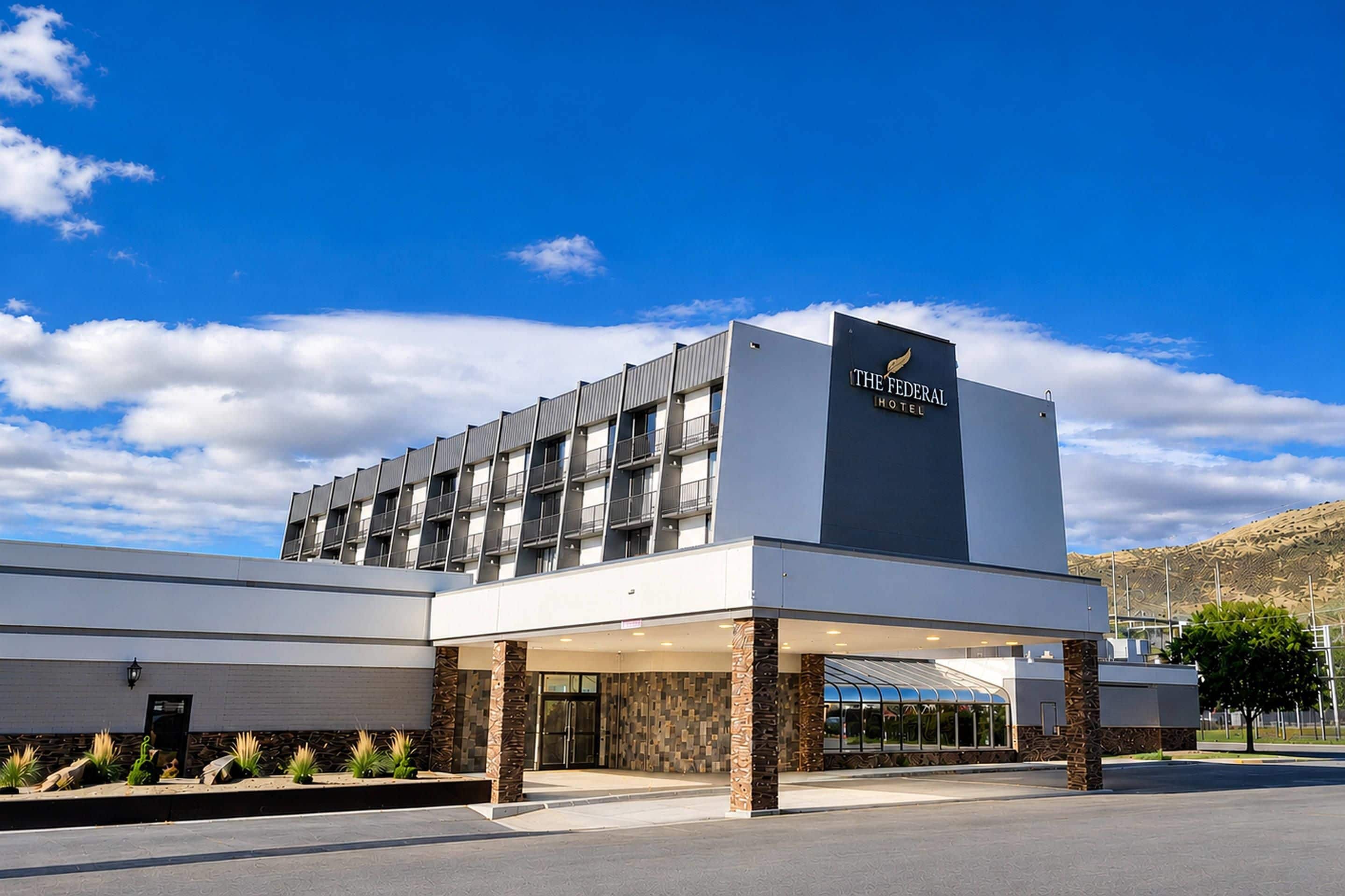 A modern hotel with a prominent sign, a covered entrance, and a landscaped area with plants.